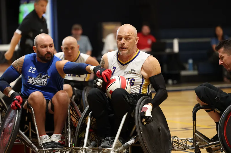A ball carrier powers between two defenders, chairs locked together