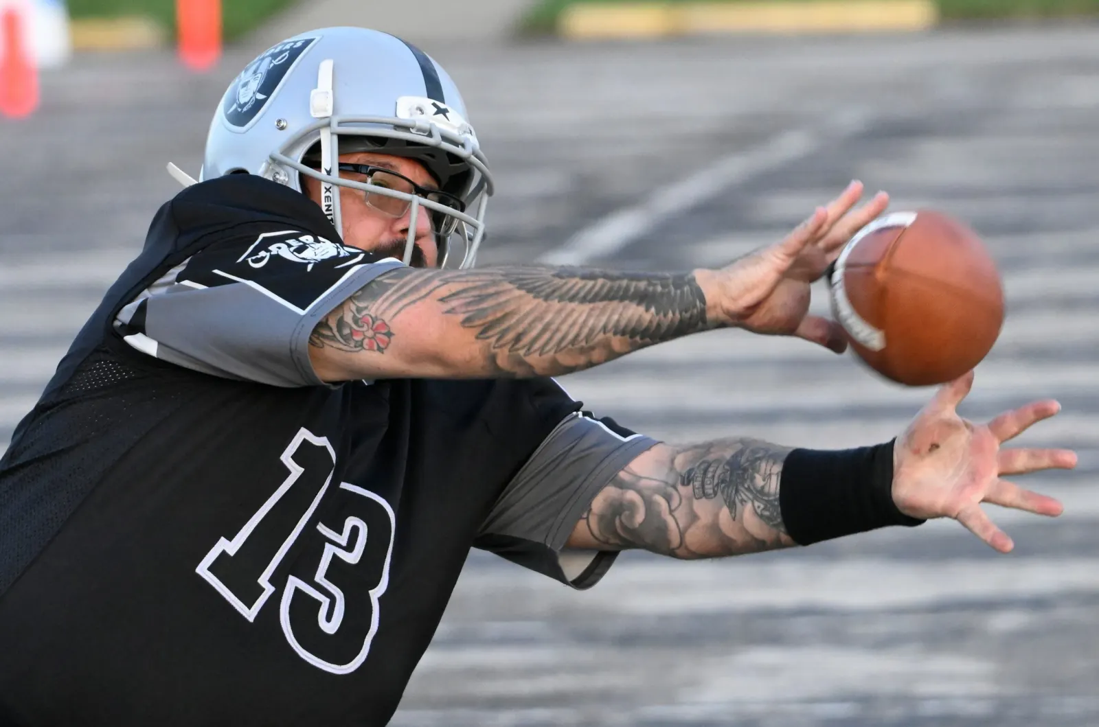 A Raiders player in a black number 13 jersey stretches both arms to reach for an incoming football.