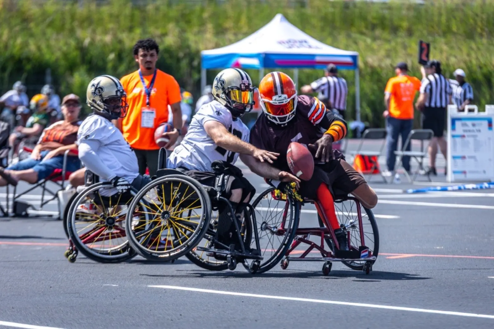 A Browns player in an orange helmet secures a low pass as two Saints defenders converge on him.