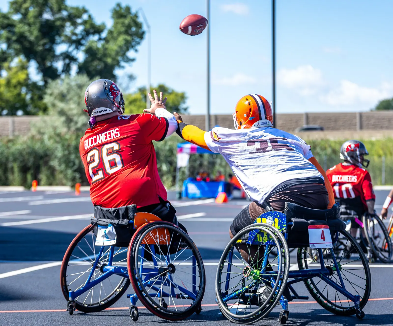 Seen from behind, a Buccaneers and a Browns player both stretch a hand toward a football spinning in the air.