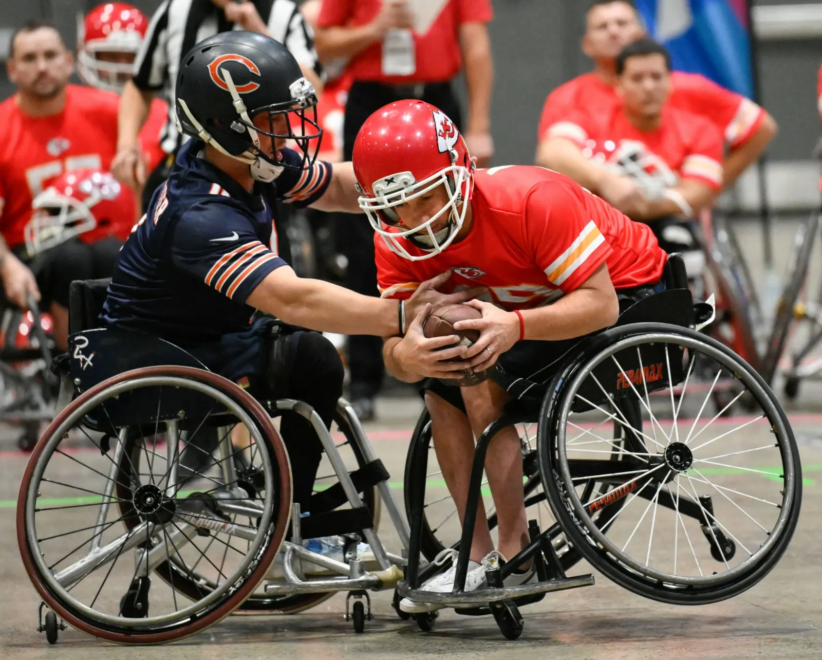 A Chicago Bears player grabs at a Kansas City ballcarrier who cradles the football as their wheelchairs lock together.