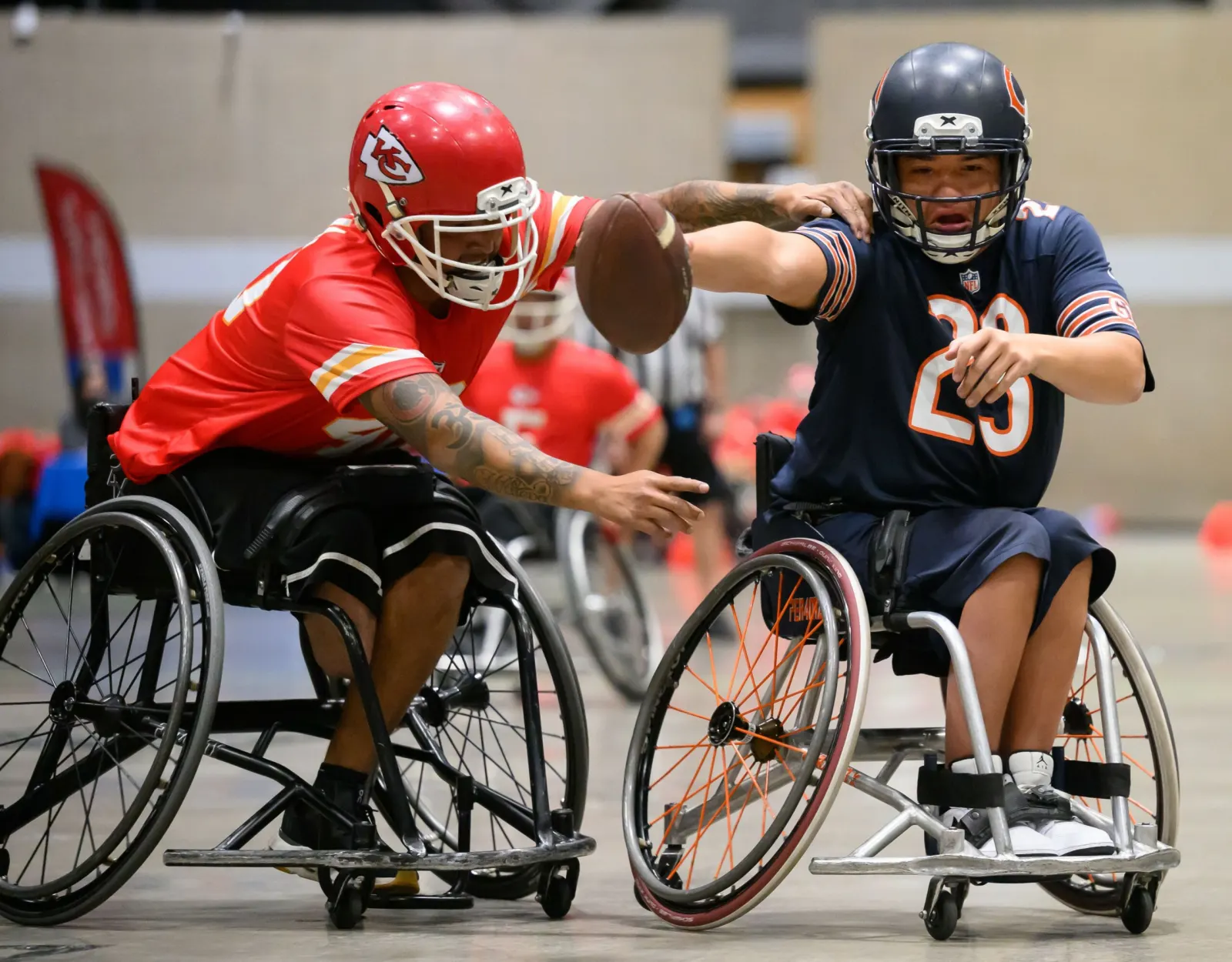 A Kansas City player in a red helmet reaches around a Chicago Bears defender to bat at the ball during play.