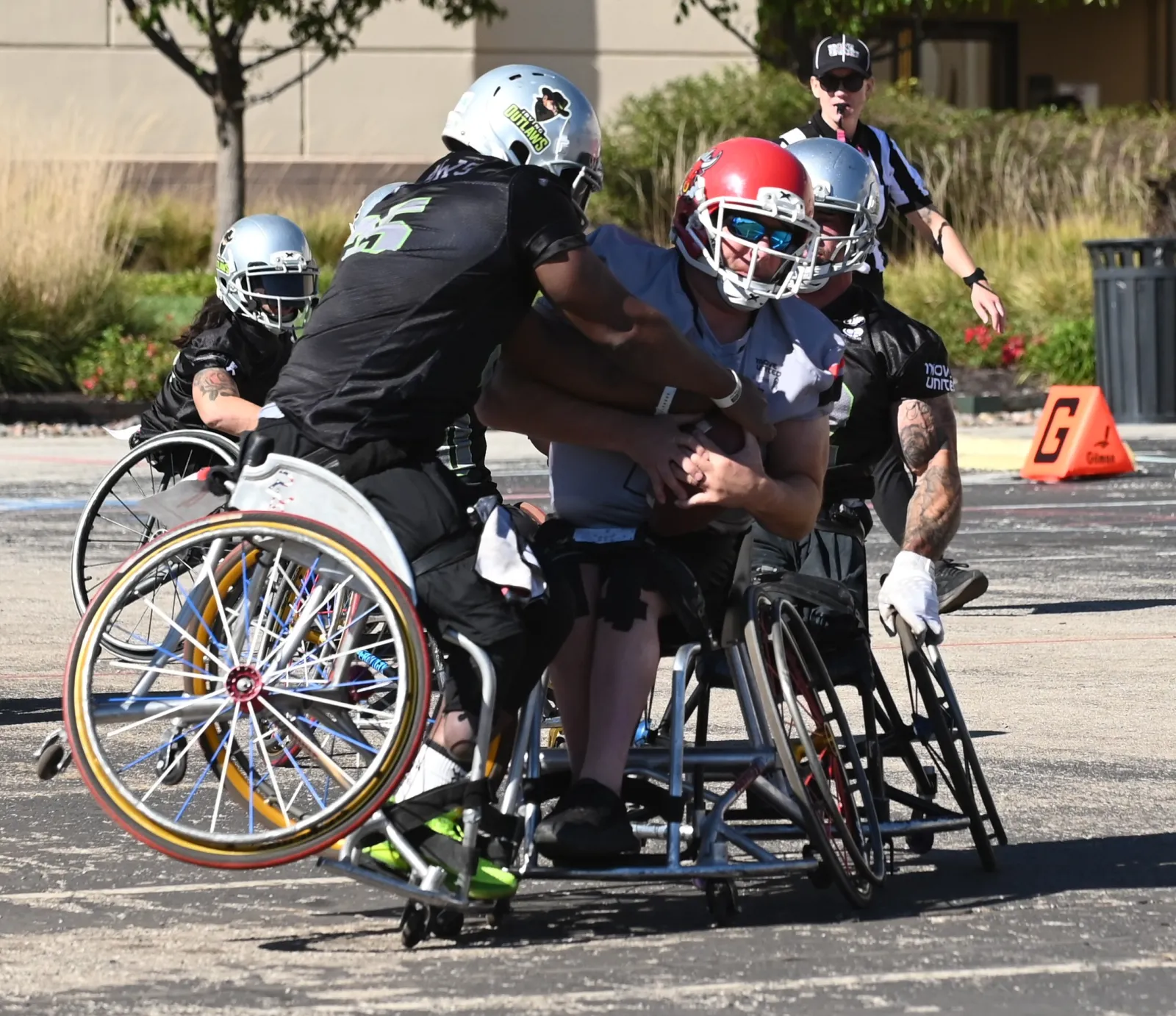 A gray-jersey ballcarrier in a red helmet clutches the football as two Irving Outlaws defenders in black wrap him up beside the orange goal-line cone marked G.