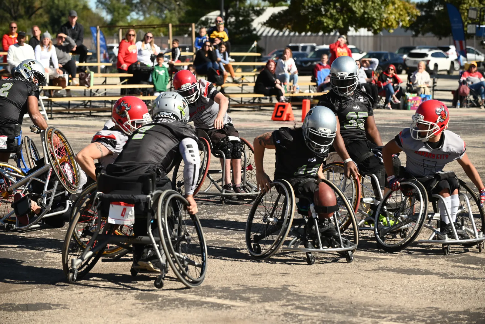 Irving Outlaws players in black jerseys and gray-jersey Kansas City players in red helmets tangle wheelchairs at the line of scrimmage near the orange goal-line cone marked G.
