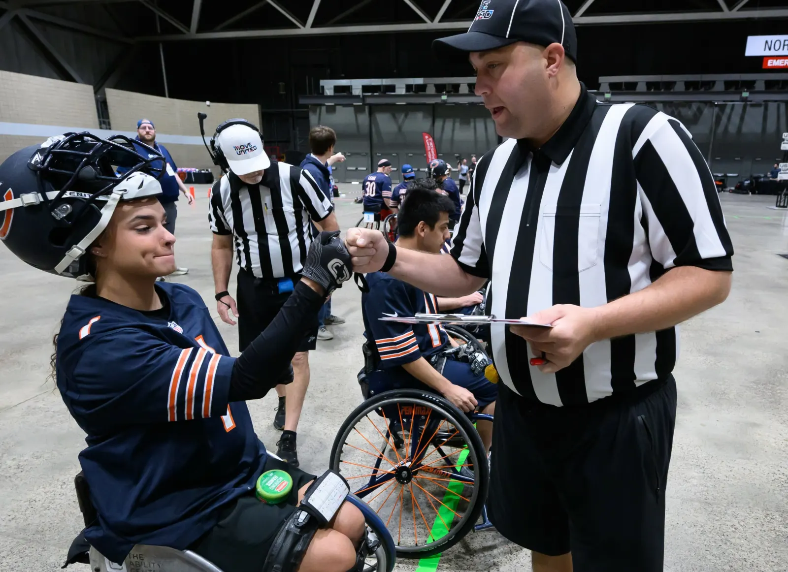 A referee with a clipboard fist-bumps a smiling Chicago player during pregame equipment check.
