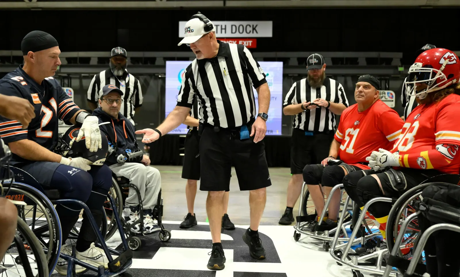 A striped-shirt referee tosses a coin between seated Chicago and Kansas City team captains before the game.