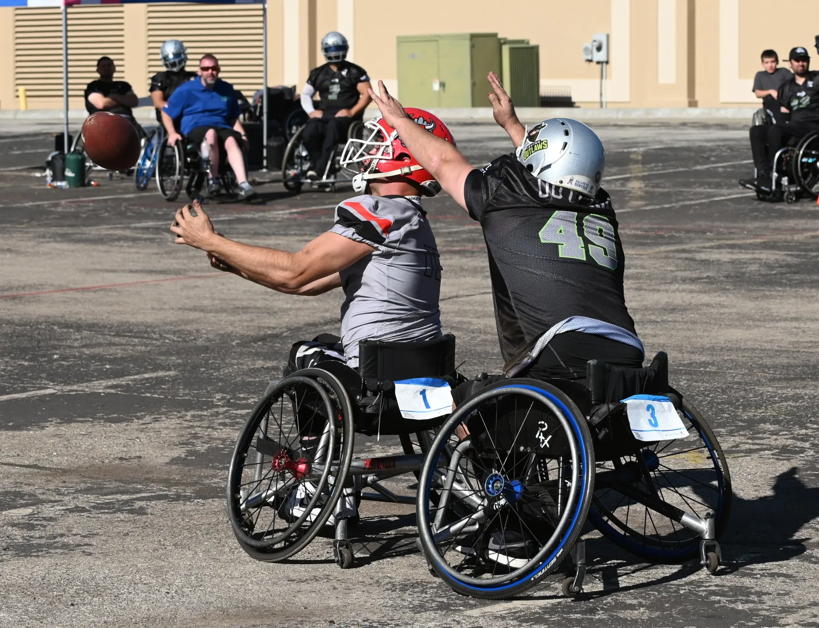 A gray-jersey, red-helmet player reaches out for an incoming football while an Irving Outlaws defender in a black number 49 jersey throws both arms up to block his view.