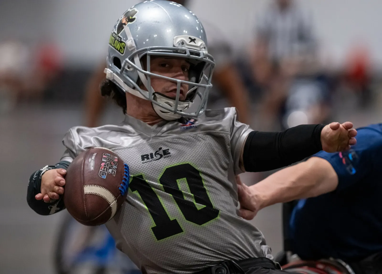 An Irving Outlaws player in a silver number 10 jersey twists sideways in his chair while clutching the football.