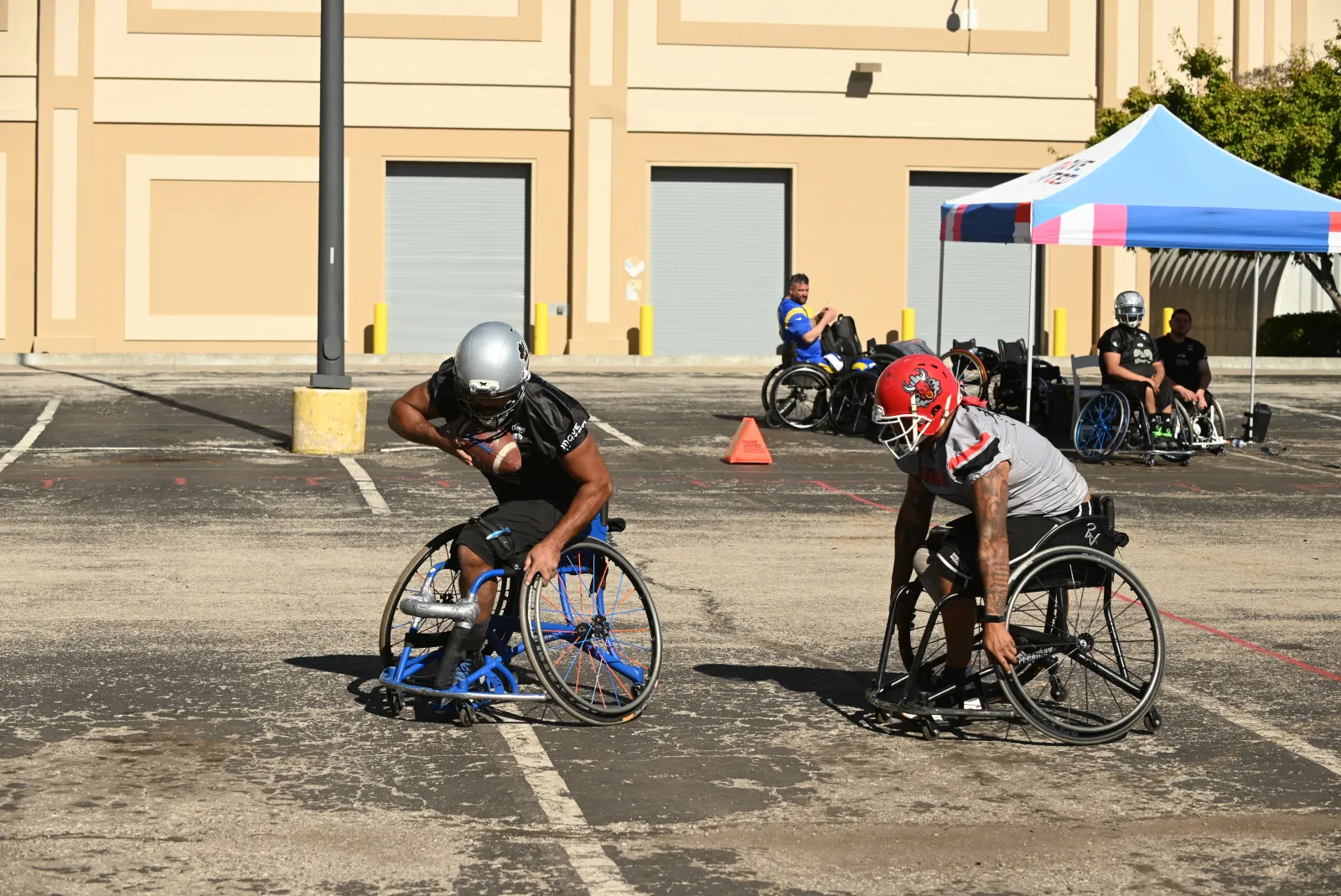 An Irving Outlaws player in a black jersey and silver helmet protects the football as a gray-jersey defender in a red bull-logo helmet chases him stride for stride across the lot.