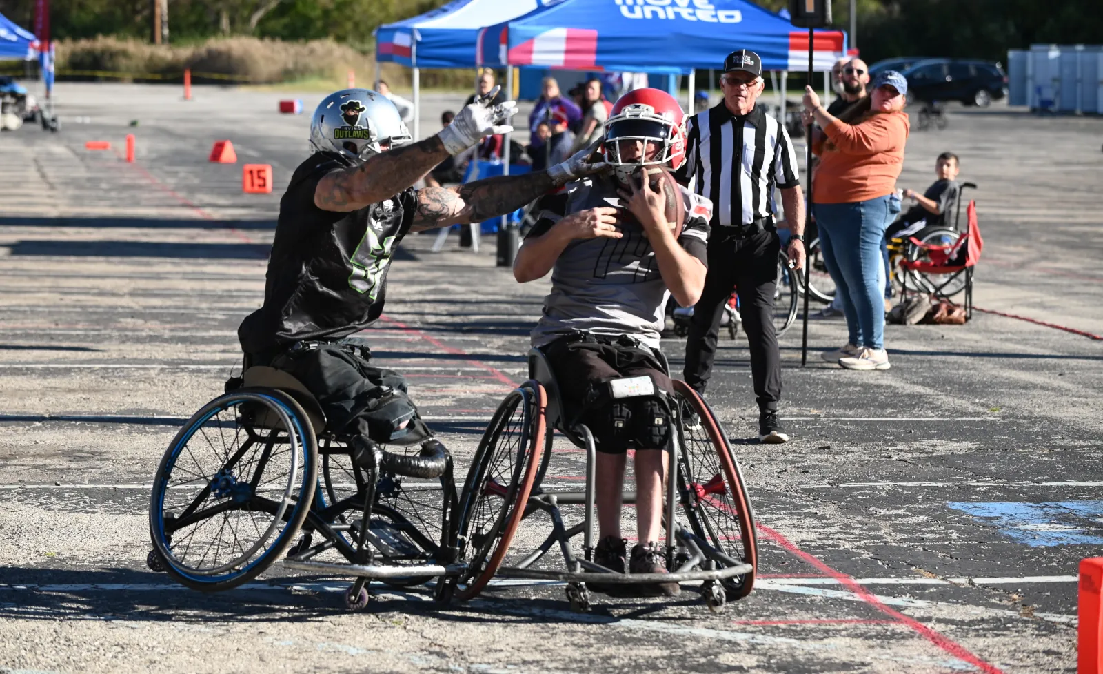 An Irving Outlaws defender in black stretches both arms toward a gray-jersey, red-helmet ballcarrier clutching the football as a striped-shirt referee watches from behind.