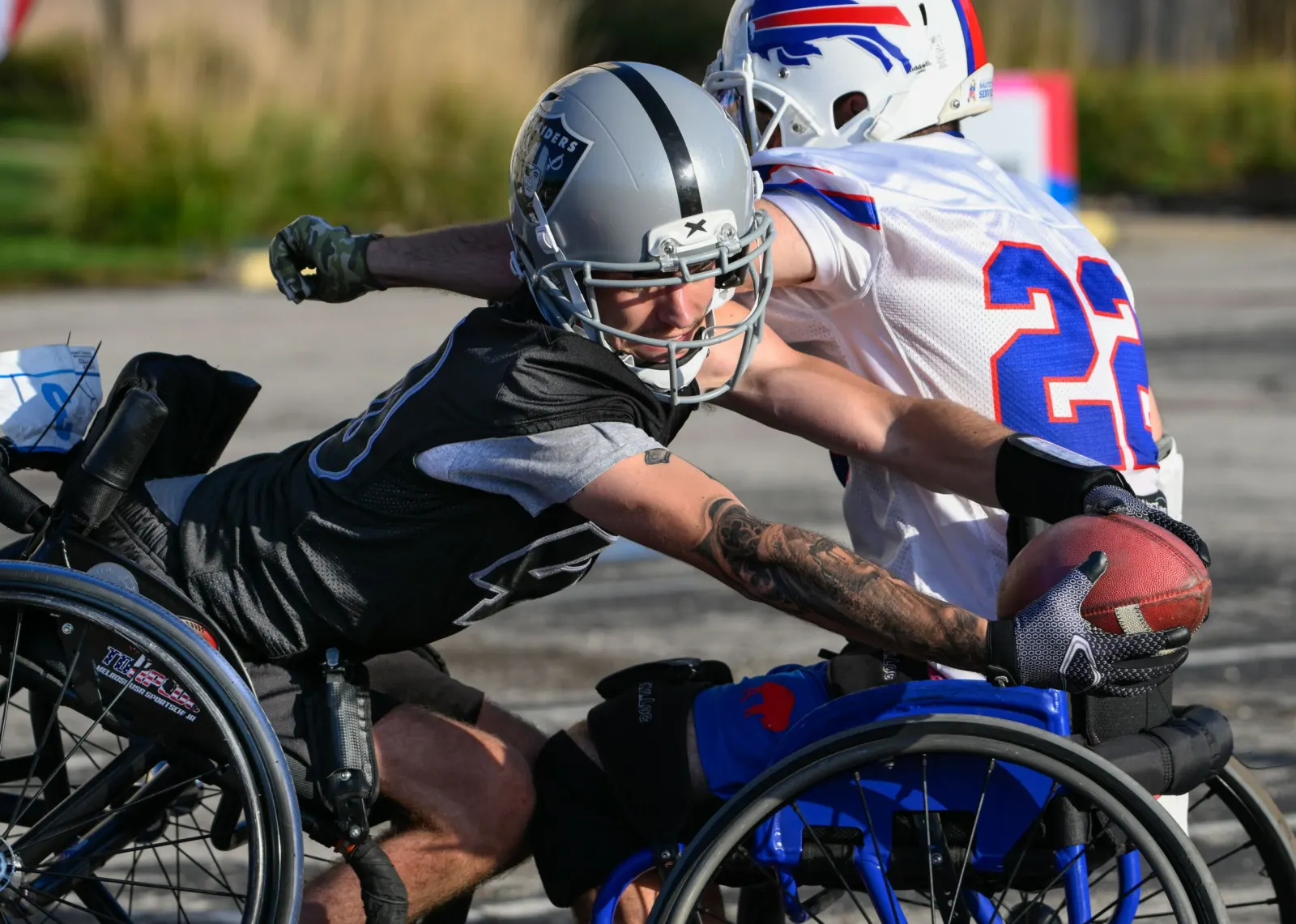 A Raiders player tips out of his chair reaching past a Bills number 22 defender for the loose football.