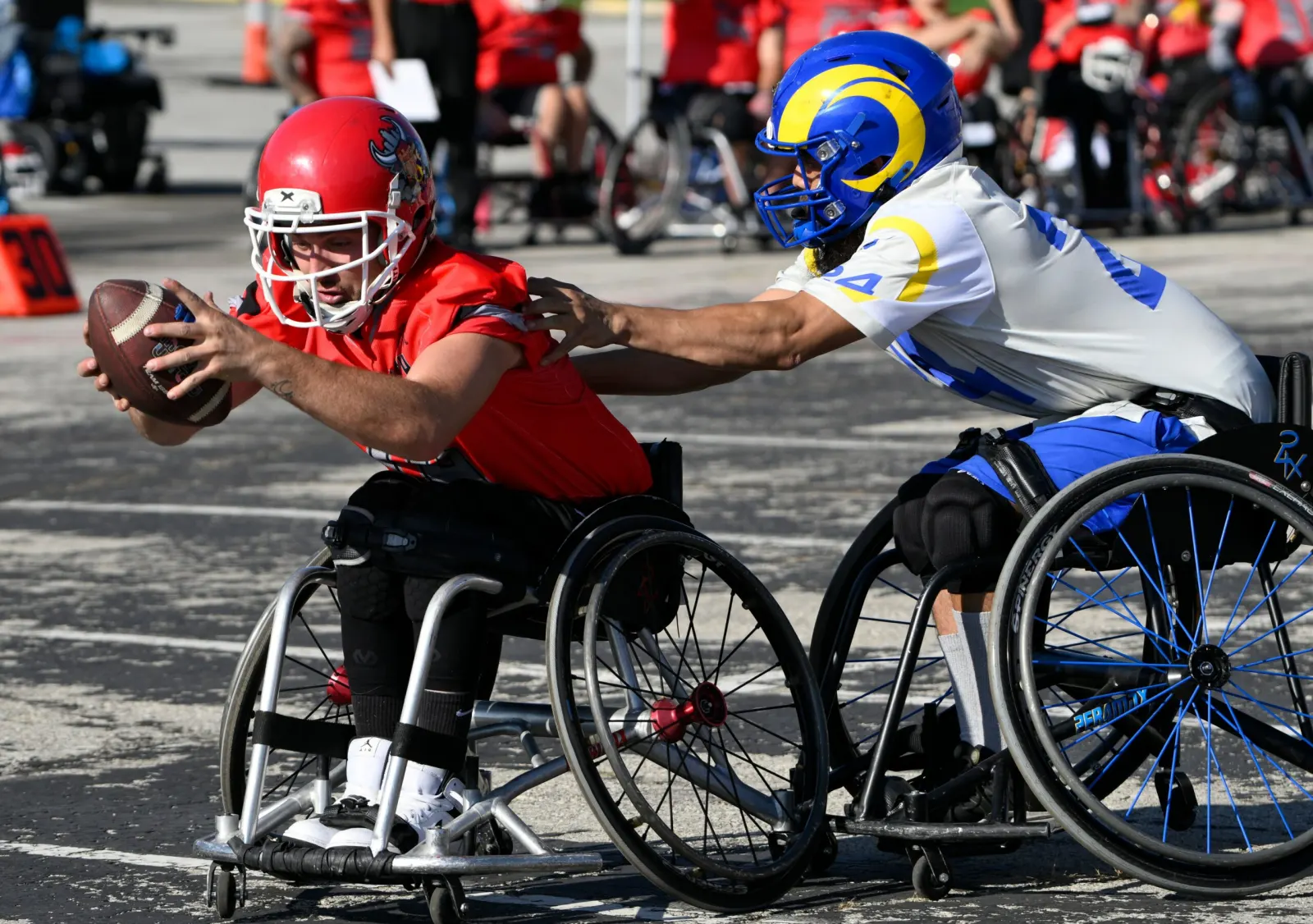 A red-jerseyed player reaches out the ball as a Rams defender in a blue-and-yellow helmet lunges to knock it away.