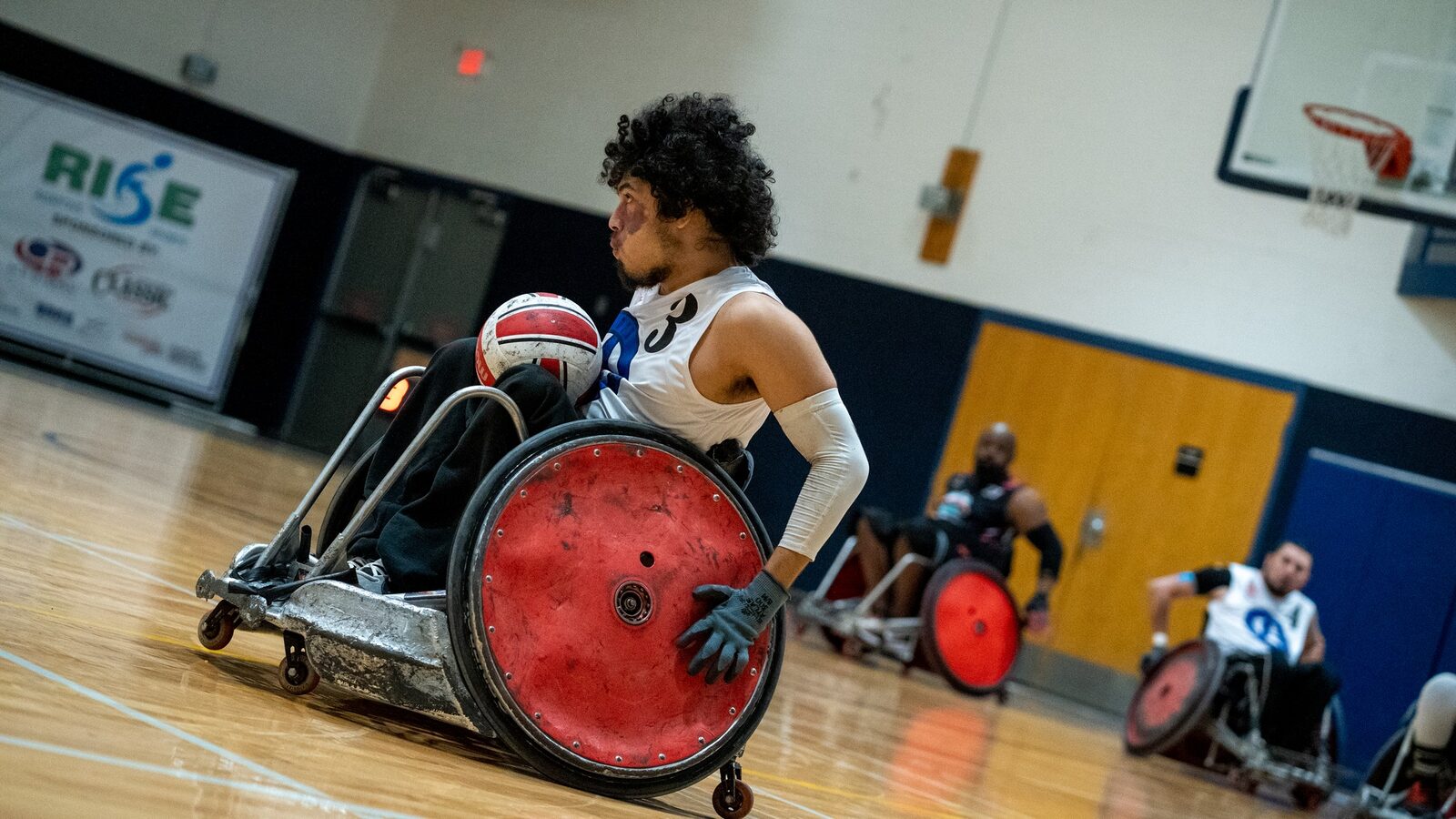 A wheelchair rugby athlete carrying the ball during a gym game.