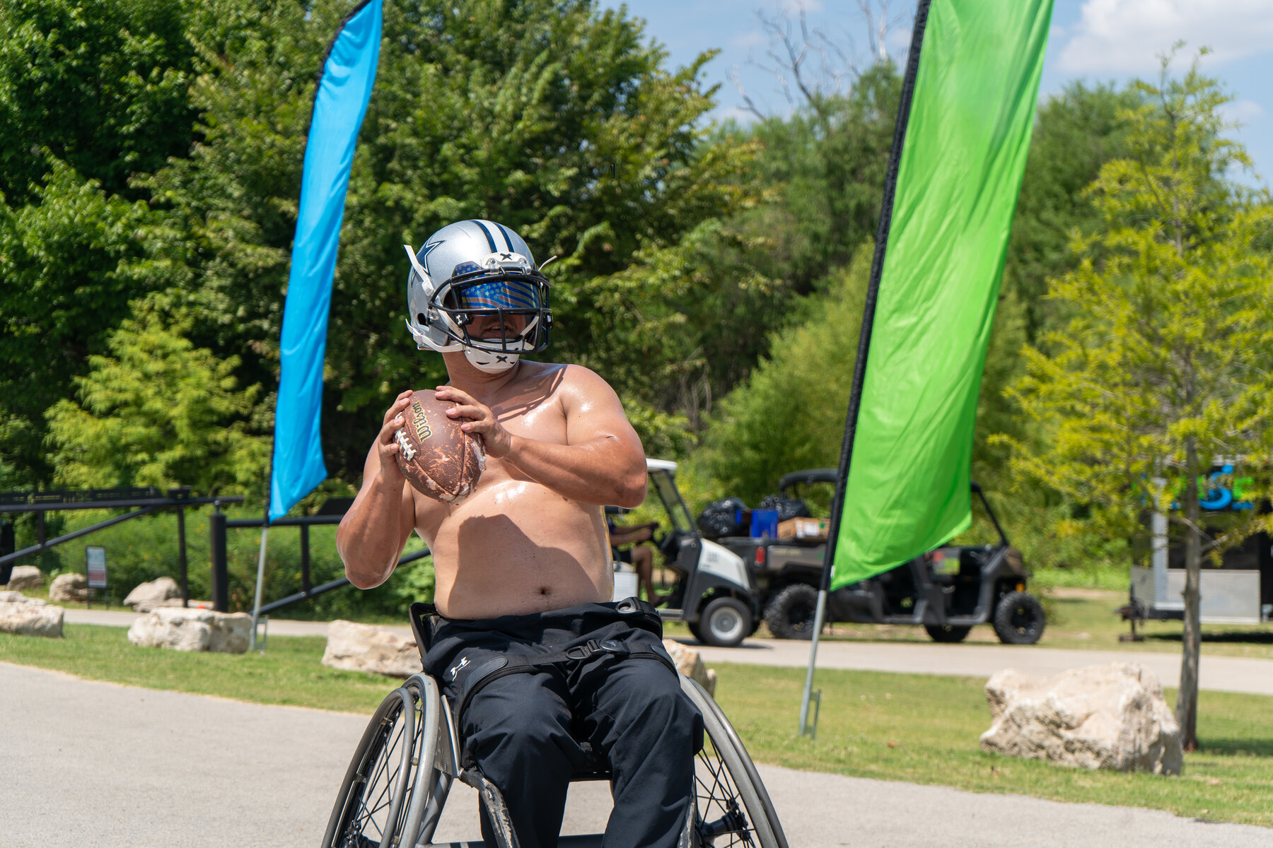 A wheelchair football player holds a football between blue and green RISE flags.