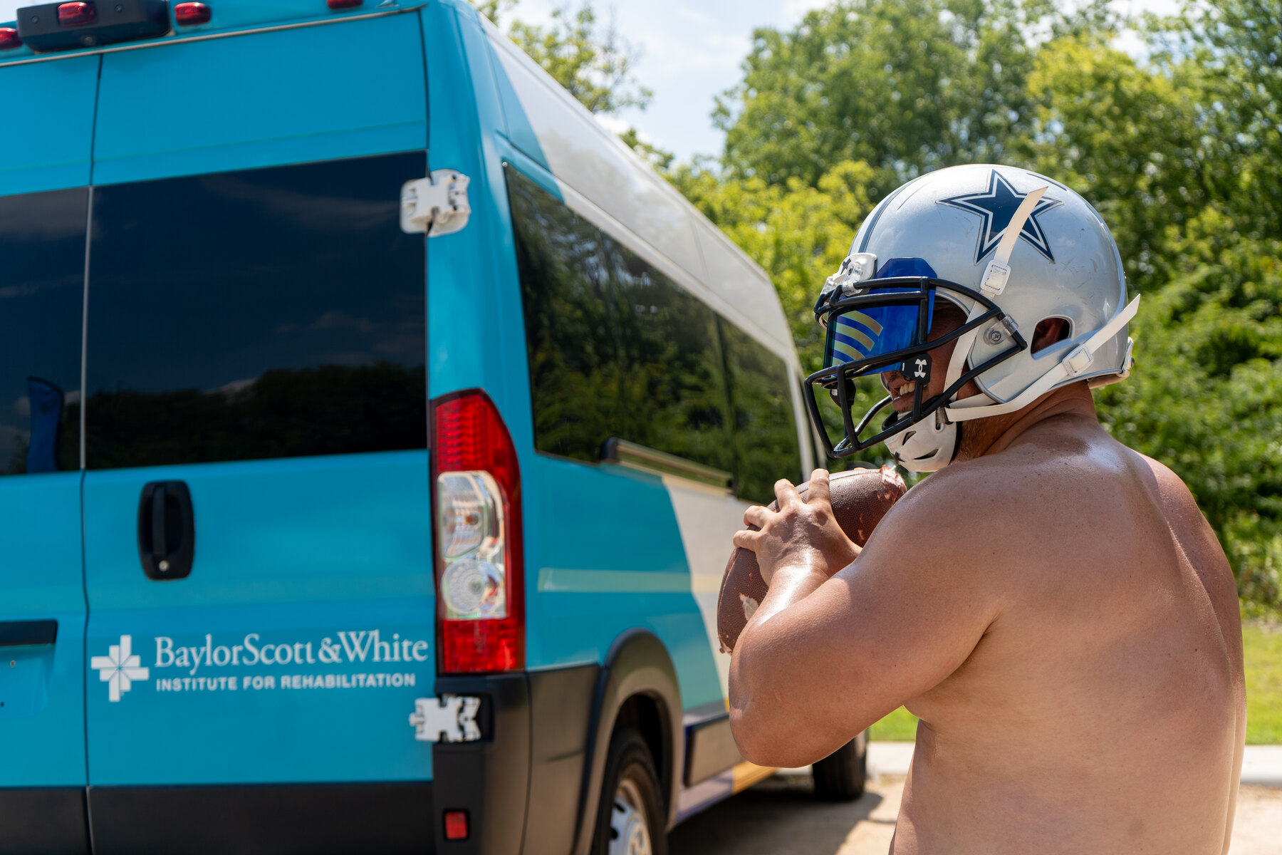 A wheelchair football player smiles while holding a football beside an adaptive sports van.